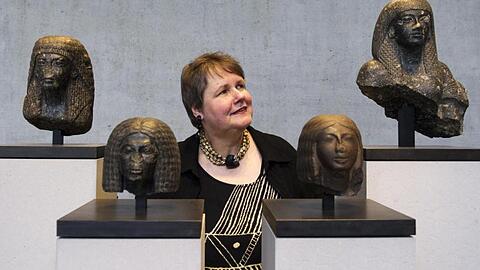 Sylvia Schoske steht zwischen vier Portraitköpfen.