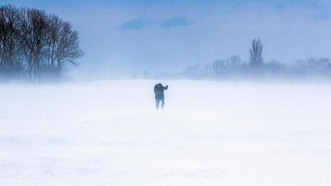 Ein Mann läuft über einen verschneiten Acker auf der Insel Rügen. Starker Wind sorgt auch hier im Norden für Schneeverwehungen.