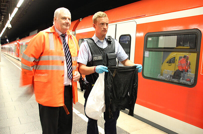 Erich Brzosa, der Leiter der DB Netz AG für den Großraum München (l.) mit einem Polizeibeamten, der die Jacke in der Hand hält, die für die Stammstreckensperrung verantwortlich ist.
