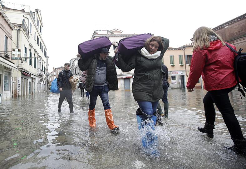 Touristen schleppen ihr Gepäck auf den Schultern durchs Hochwasser.