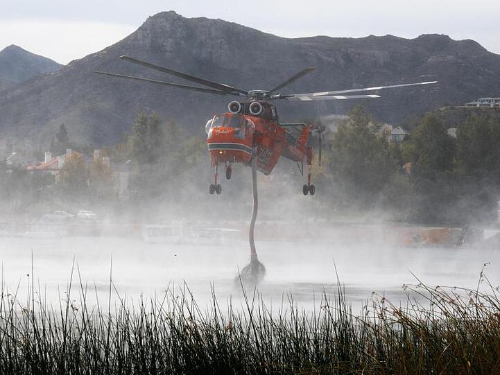 Ein Hubschrauber zieht während eines Löscheinsatzes Wasser aus einem See. Seit Donnerstag sind mehrere Tausend Feuerwehrleute im Einsatz, um die Flammen im Norden und im Süden zu bekämpfen.
