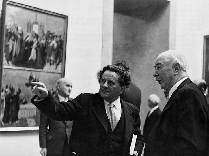 Bei der Wiedereröffnung der Alten Pinakothek 1957 zeigt der vier Jahre zuvor wieder eingesetzte Generaldirektor Ernst Buchner dem Bundespräsidenten und großen Kunstfreund Theodor Heuss die Höhepunkte der Sammlung. Buchner, ab Mai 1933 NSDAP-Mitglied, war von März 1933 bis 1945 verantwortlich für die Pinakotheken.