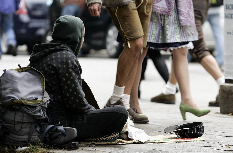 Münchner Kontraste: Während ein Paar in Tracht durch die Innenstadt spaziert, bettelt ein Obdachloser am Boden um etwas Geld.