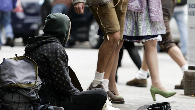 Münchner Kontraste: Während ein Paar in Tracht durch die Innenstadt spaziert, bettelt ein Obdachloser am Boden um etwas Geld. Münchner Kontraste: Während ein Paar in Tracht durch die Innenstadt spaziert, bettelt ein Obdachloser am Boden um etwas Geld.