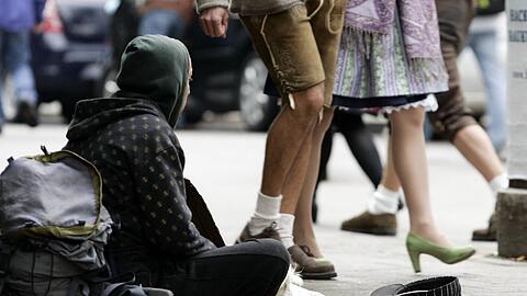 Münchner Kontraste: Während ein Paar in Tracht durch die Innenstadt spaziert, bettelt ein Obdachloser am Boden um etwas Geld.