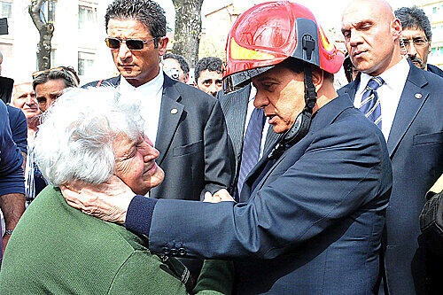 Silvio Berlusconi (hier mit Helm) tröstet vor Ort in L'Aquila eine ältere Frau.