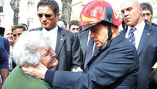 Silvio Berlusconi (hier mit Helm) tröstet vor Ort in L'Aquila eine ältere Frau.