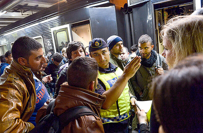 Flüchtlinge mit einem schwedischen Polizisten am Stockholmer Bahnhof. Das Land führt vorübergehend wieder Grenzkontrollen ein.