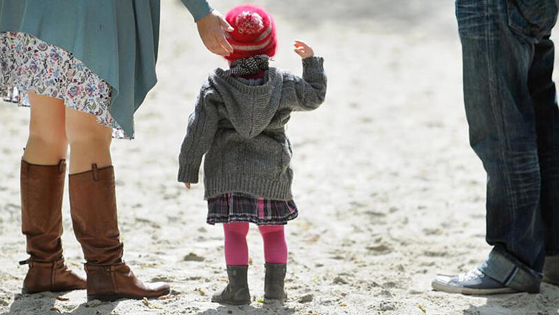 Ein Kind steht auf einem Spielplatz zwischen seinen Eltern. Ein unverheirateter Mann kann nicht die Kinder seiner Lebensgefährtin adoptieren.