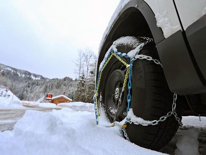 Ein Auto mit aufgezogenen Schneeketten steht an der Zufahrt des gesperrten Riedbergpasses.