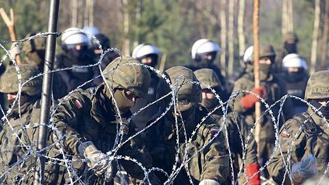 Polnische Polizisten und Grenzschützer stehen in Grodno am Stacheldrahtzaun.