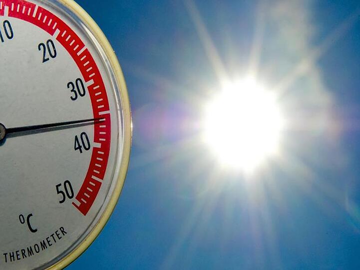 Ein Thermometer zeigt fast 36 Grad Celsius an - im Hintergrund blauer Himmel und Sonne. Foto: Patrick Pleul/Archivbild
