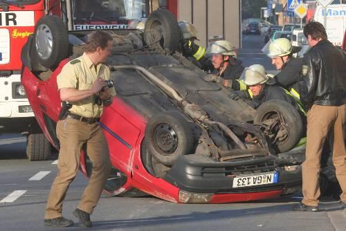 Feuerwehrmänner stemmen sich gegen das Auto, um es wieder auf die Räder zu stellen.