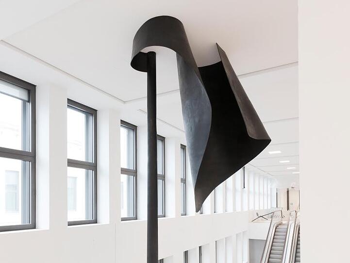 Die Bronze-Skulptur in Form einer zweigeteilten Flagge auf halbmast ist im zentralen Treppenhaus des Humboldt Forums zu sehen.