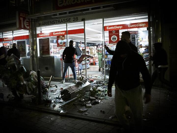 Menschen stehen in der Krawallnacht vor einem geplünderten Geschäft in der Stuttgarter Innenstadt.