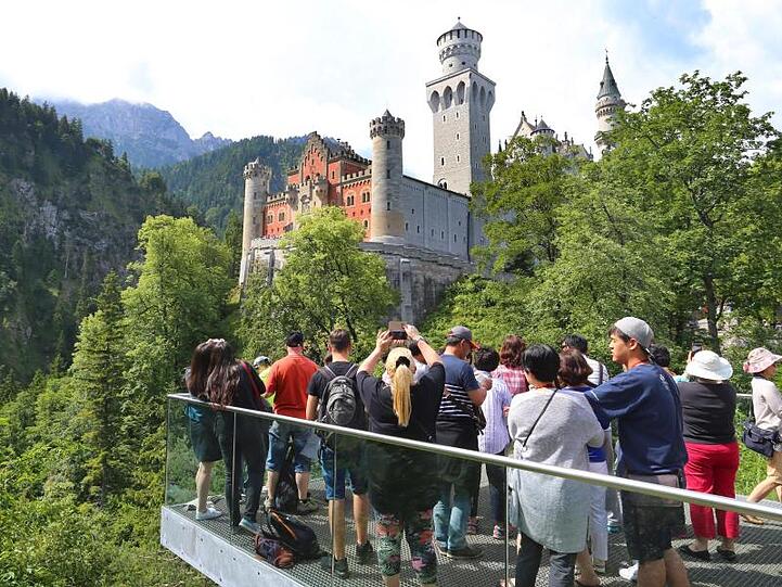 Touristen stehen auf einer Aussichtsplattform unterhalb des Schlosses Neuschwanstein. Foto: Karl-Josef Hildenbrand/dpa/Archivbild