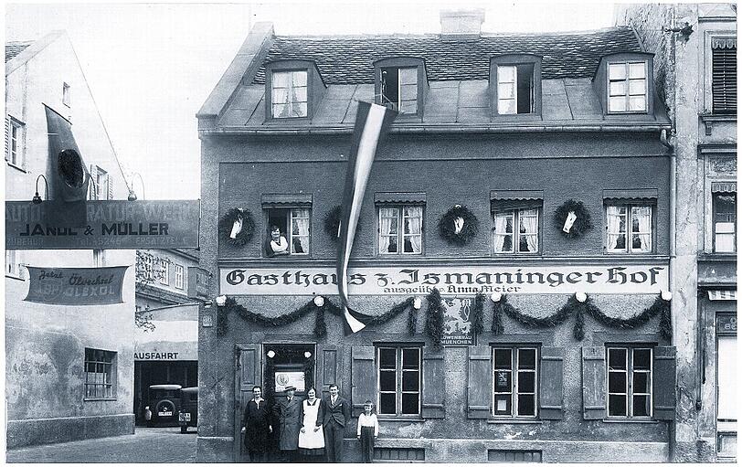 Das Gasthaus Ismaninger Hof um 1930 mit Festschmuck und Wirtsfamilie in der Ismaninger Straße 38. Hier konnte man ein frisches Löwenbräu trinken. Nebenan, bei Jandl & Müller, wurden Autos repariert.