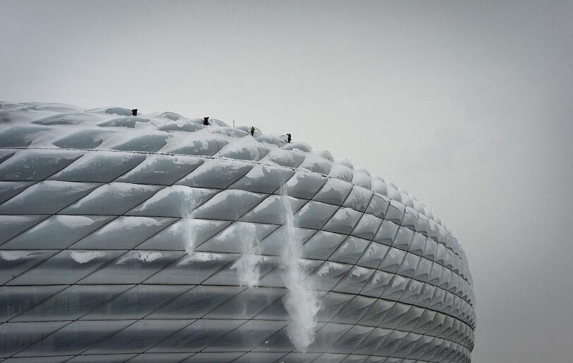 Angeseilte Kletterer schaufeln die Außenhaut der Allianz Arena frei.