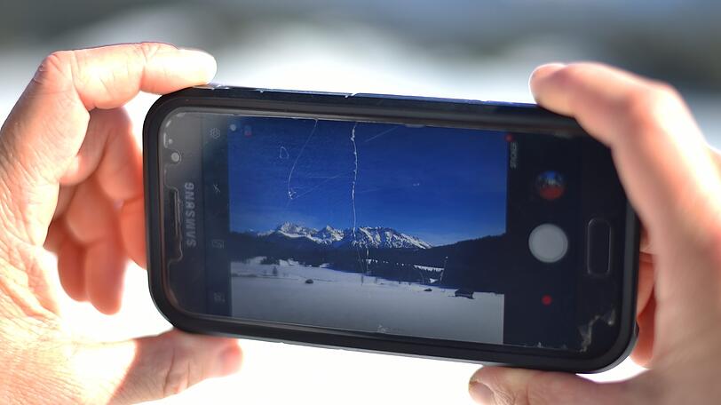 Gerold: Eine Frau fotografiert mit ihrem Smartphone den mit Eis bedeckten Geroldsee vor dem Karwendel-Gebirge.