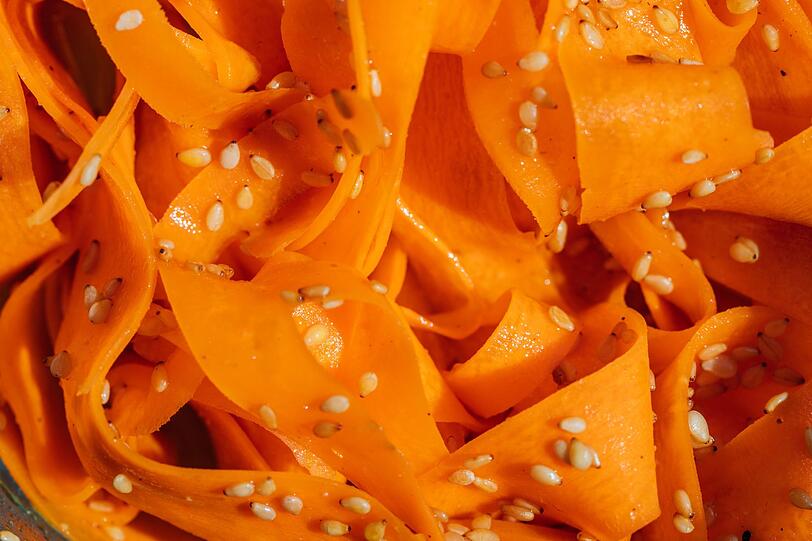 F&uuml;r das Dressing des Carrot-Ribbon-Salads verr&uuml;hren Sie zwei EL Reisessig, einen EL Sesam&ouml;l, einen TL Honig sowie einen TL Sojaso&szlig;e. F&uuml;r etwas Sch&auml;rfe mischen Sie einen halben Teel&ouml;ffel Chiliflocken unter. Danach heben Sie zwei Essl&ouml;ffel grob gehackte Erdn&uuml;sse oder Sesam sowie zwei in feine Ringe geschnittene Fr&uuml;hlingszwiebeln unter. Vor dem Servieren sollte der Salat mindestens 15 Minuten ziehen, damit die Karotten etwas weicher werden und die Aromen sich entfalten.
