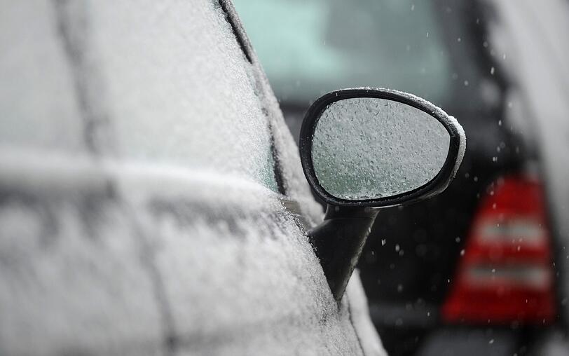Mit weißem Schnee bepudert steht ein Auto in der Münchner Innenstadt.