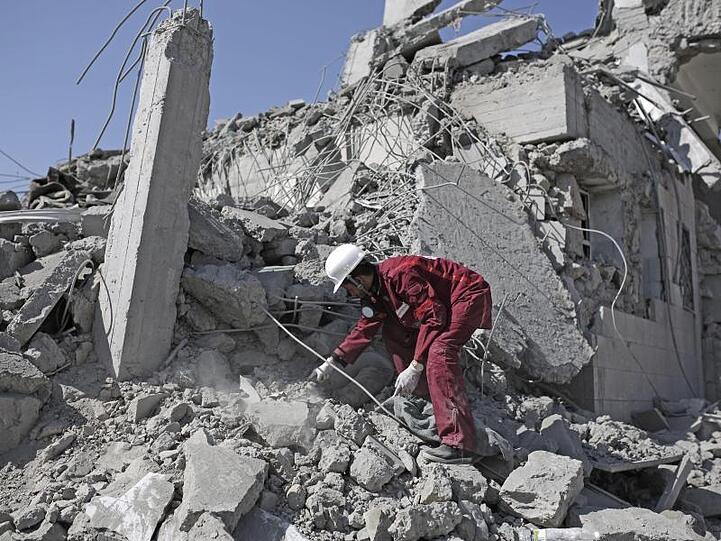 Eine Rettungskraft sucht in den Trümmern eines Gefangenenlagers nach verschütteten Leichen.