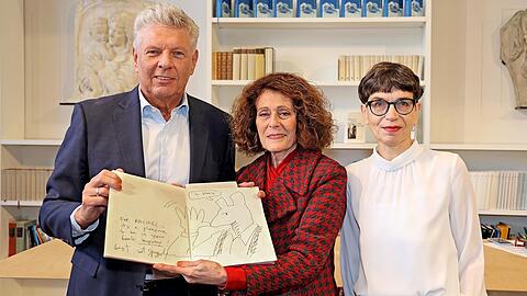 Dieter Reiter, Rachel Salamander und Anke Buettner in der Monacensia mit dem Gästebuch der Literaturhandlung. Die aufgeschlagene Seite zeigt eine Zeichnung von Art Spiegelman, die auf Henry Kissingers Eintrag auf der Seite davor reagiert.