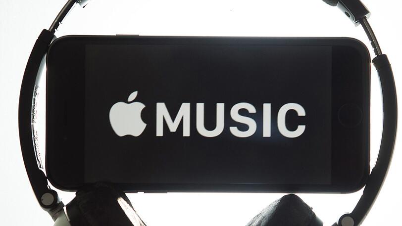 Ein Kopfhörer umgibt ein iPhone mit dem Schriftzug "Apple Music".