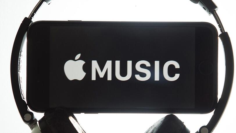 Ein Kopfhörer umgibt ein iPhone mit dem Schriftzug "Apple Music". Ein Kopfhörer umgibt ein iPhone mit dem Schriftzug "Apple Music".