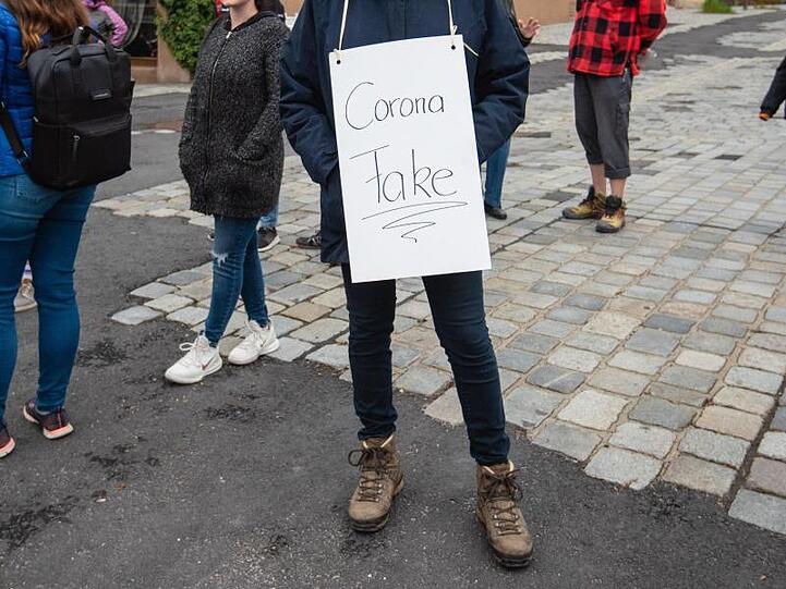 Eine Teilnehmerin trägt bei einer Demo gegen die Corona-Maßnahmen ein Schild mit der Aufschrift "Corona Fake".
