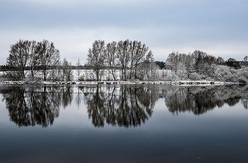 Winteridyll in Bayern: Die schneebedeckten Bäume am Hagenheimer Weiher bei Hagenheim spiegeln sich im Wasser.