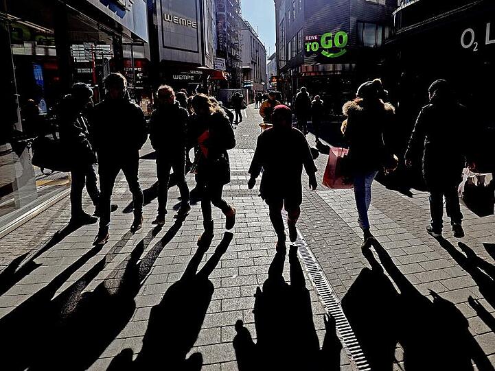 Passanten werfen in einer Kölner Fußgängerzone lange Schatten.
