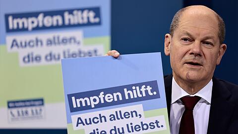 Bundeskanzler Olaf Scholz präsentiert ein Plakat aus der neuen Impfkampagne.