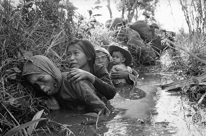 Frauen und Kinder kauern in einem matschigen Kanal, um sich vor dem starken Feuerbeschuss des Vietkongs in Bao Trai, 20 Meilen westlich von Saigon, zu schützen.