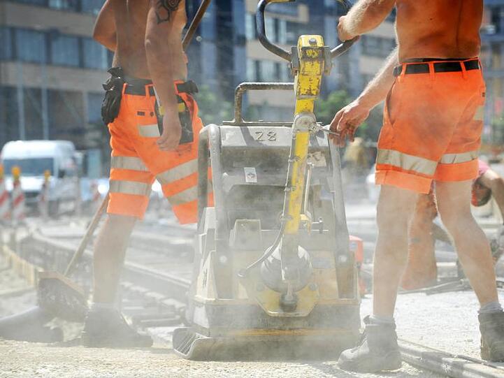 Straßenarbeiter befestigen bei großer Hitze mit einem Rüttler den Staßenbelag. Foto: Frank Leonhardt/Archiv
