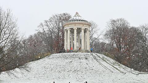 Spaziergänger laufen vor dem Monopteros durch den verschneiten Englischen Garten.