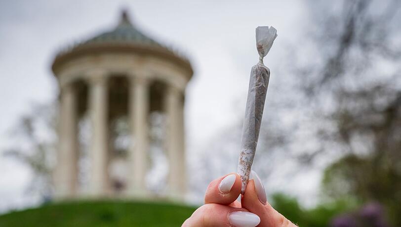 Eine Frau hält einen Joint vor der Kulisse des Monopteros im Englischen Garten.