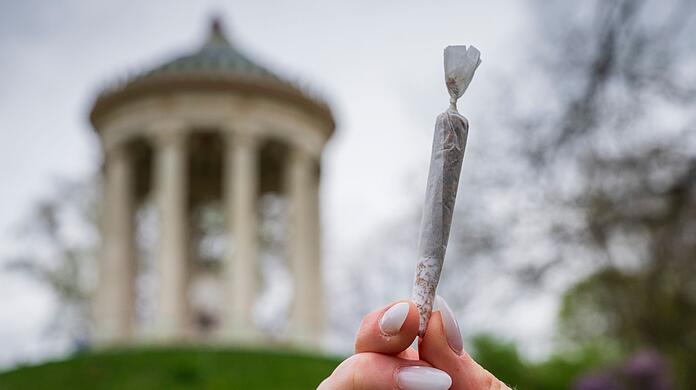 Eine Frau hält einen Joint vor der Kulisse des Monopteros im Englischen Garten.