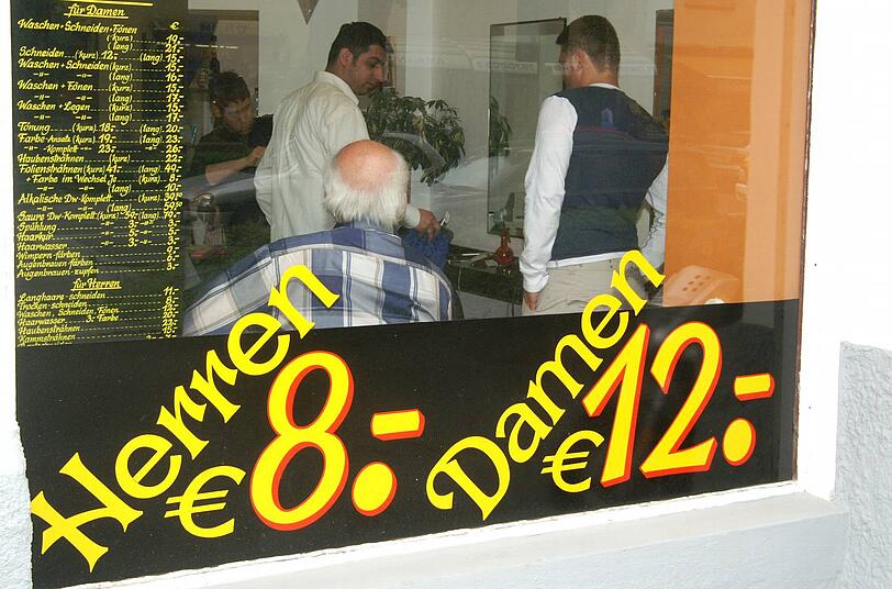 "Herren acht Euro, Damen zwölf" steht an diesem Friseurfenster. Warum Frauen hier mehr zahlen, ist historisch bedingt, sagen Experten.
