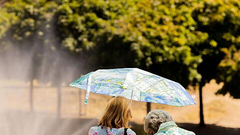 Zwei Frauen schützen mit einem Regenschirm vor der Sonne.