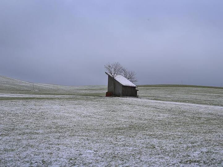 Ein Stadel steht inmitten der leicht mit Schnee bedeckten Allgäuer Landschaft. Foto: Karl-Josef Hildenbrand