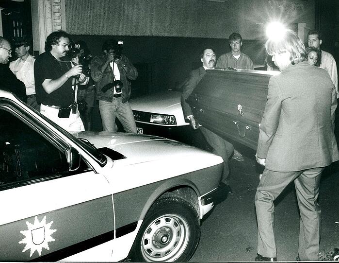 Der Abend nach dem Mord: Am Sonntag, den 15. Juli 1990, wird der Tote entdeckt. Von Journalisten beobachtet, bringen Bestatter den Toten in die Rechtsmedizin.