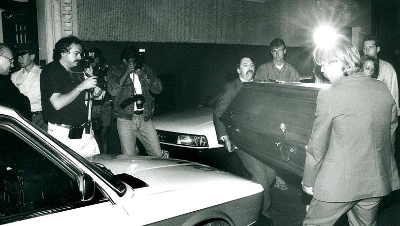 Der Abend nach dem Mord: Am Sonntag, den 15. Juli 1990, wird der Tote entdeckt. Von Journalisten beobachtet, bringen Bestatter den Toten in die Rechtsmedizin.