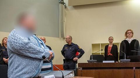 Der Angeklagte (l) steht zum Prozessauftakt an seinem Platz im Gericht.