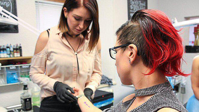 Die Tätowiererin begutachtet die Tattoo-Vorlage auf Danielas Unterarm.