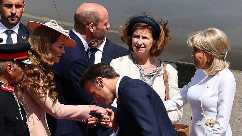 Mit einem Handkuss hat Emmanuel Macron Prinzessin Kate nach seiner Ankunft in Großbritannien begrüßt. Im Hintergrund schütteln sich Prinz William und Brigitte Macron die Hände.