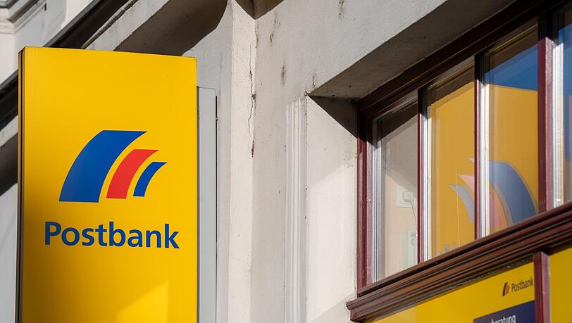 Ein Schild mit dem Logo der Postbank ist an der Fassade einer Bankfiliale angebracht.