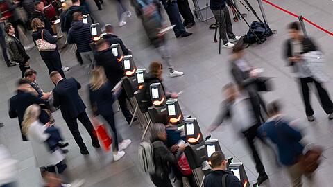Besucher einer Messe gehen im Eingangsbereich durch die elektronische Einlasskontrolle.