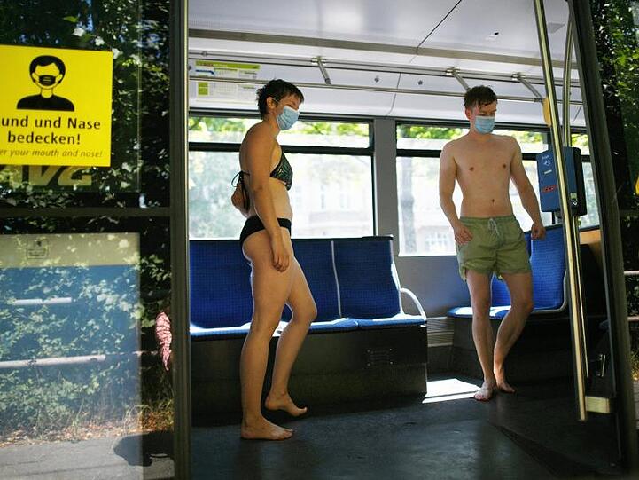 Eisbachschwimmer tragen Mund-Nasenschutz und stehen an der Tramhaltestelle Tivolistraße in der Tram. Foto: Angelika Warmuth/dpa
