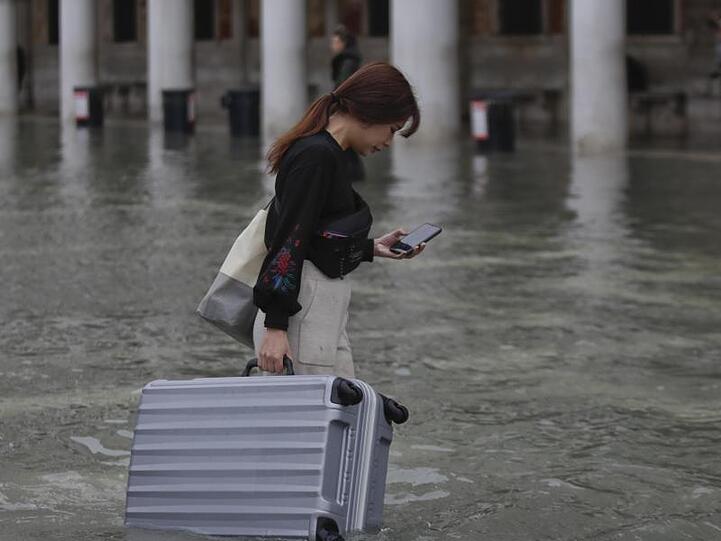 Eine Touristin trägt ihr Gepäck durch das Hochwasser auf dem Markusplatz.